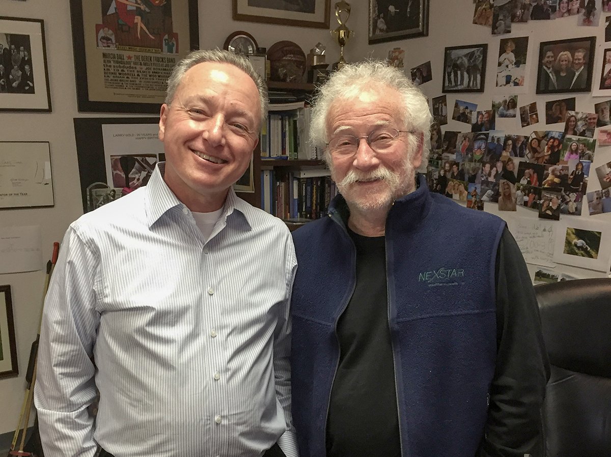 Byron Hewett, left, and Larry Gold smiling in an office filled with books and photographs