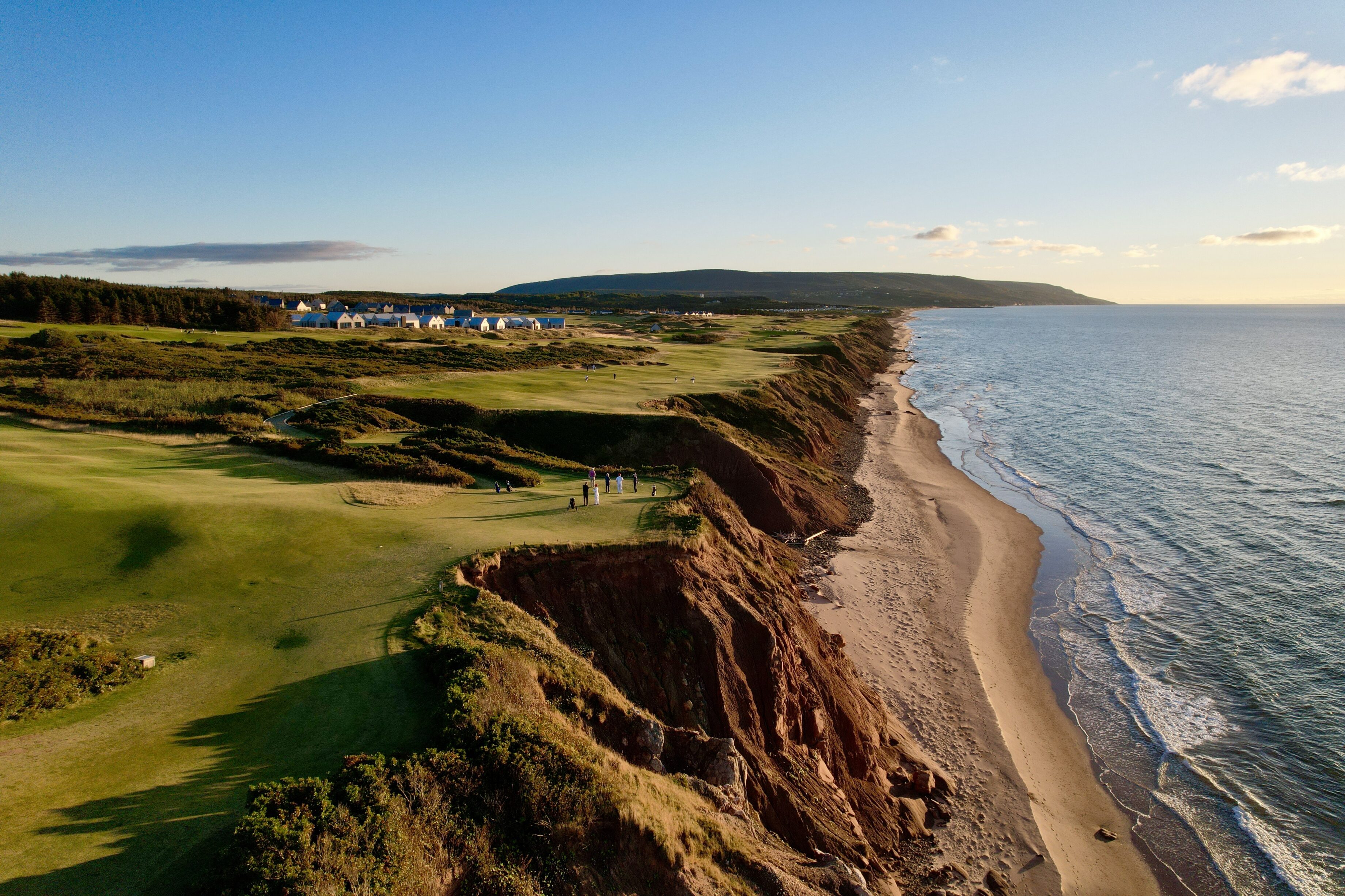 Golfers playing beside the red cliffs and blue water at Cabot Cape Breton