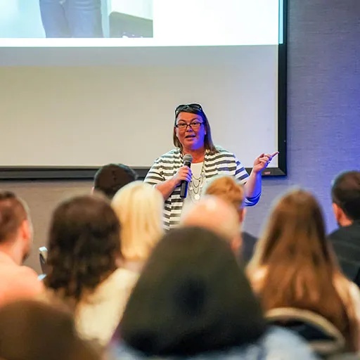 A speaker holding a microphone addresses seated attendees at a Cadmium conference gathering