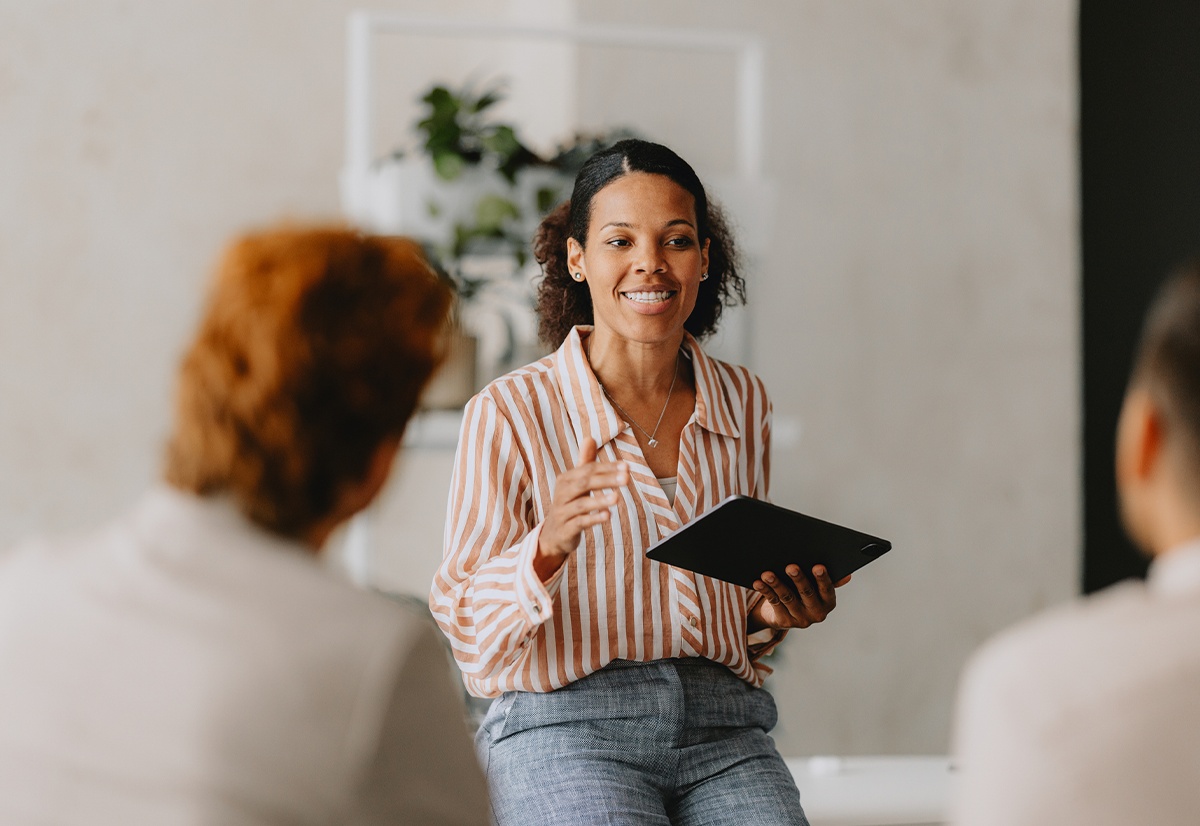 A woman holding a tablet speaks with two colleagues in an office.