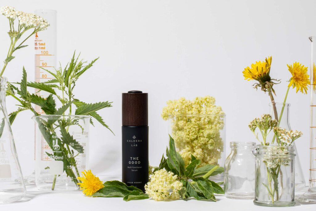 Original The Good serum bottle surrounded by botanicals and laboratory glassware