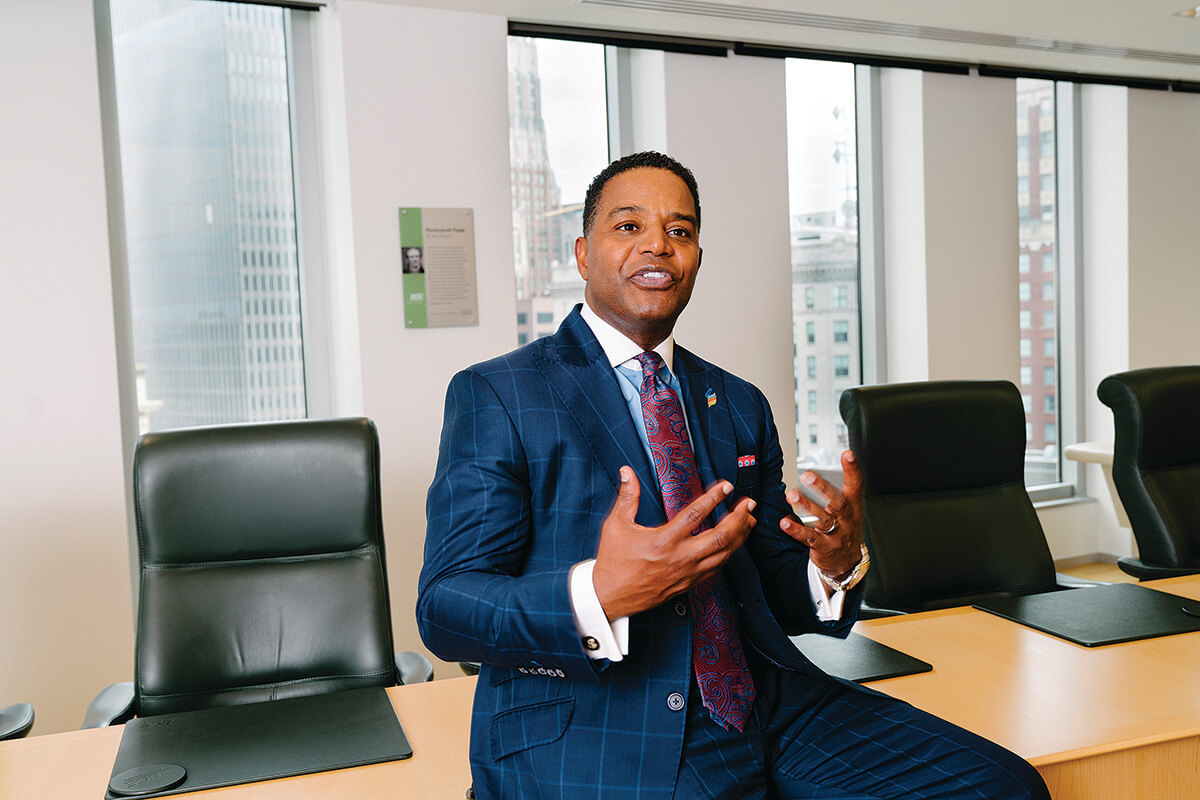 Calvin Butler seated on the edge of a conference table, gesturing during a conversation.