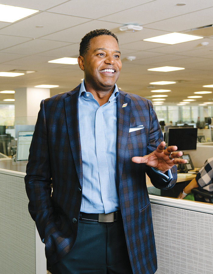Calvin Butler speaking in an open office, wearing a checked jacket and blue shirt.