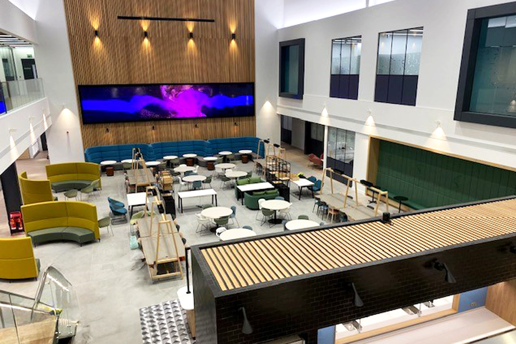 The shared atrium at CDP’s Bourn Quarter headquarters, with tables and colorful seating