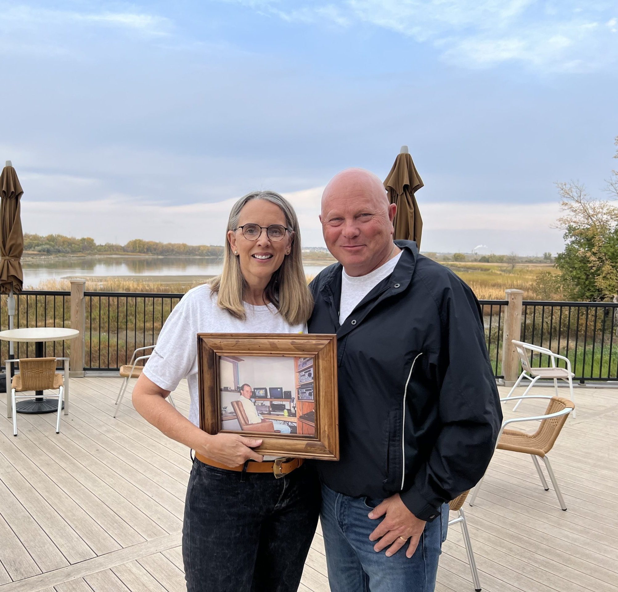 Candace Muggerud and Todd Muggerud standing outdoors while holding a framed photograph
