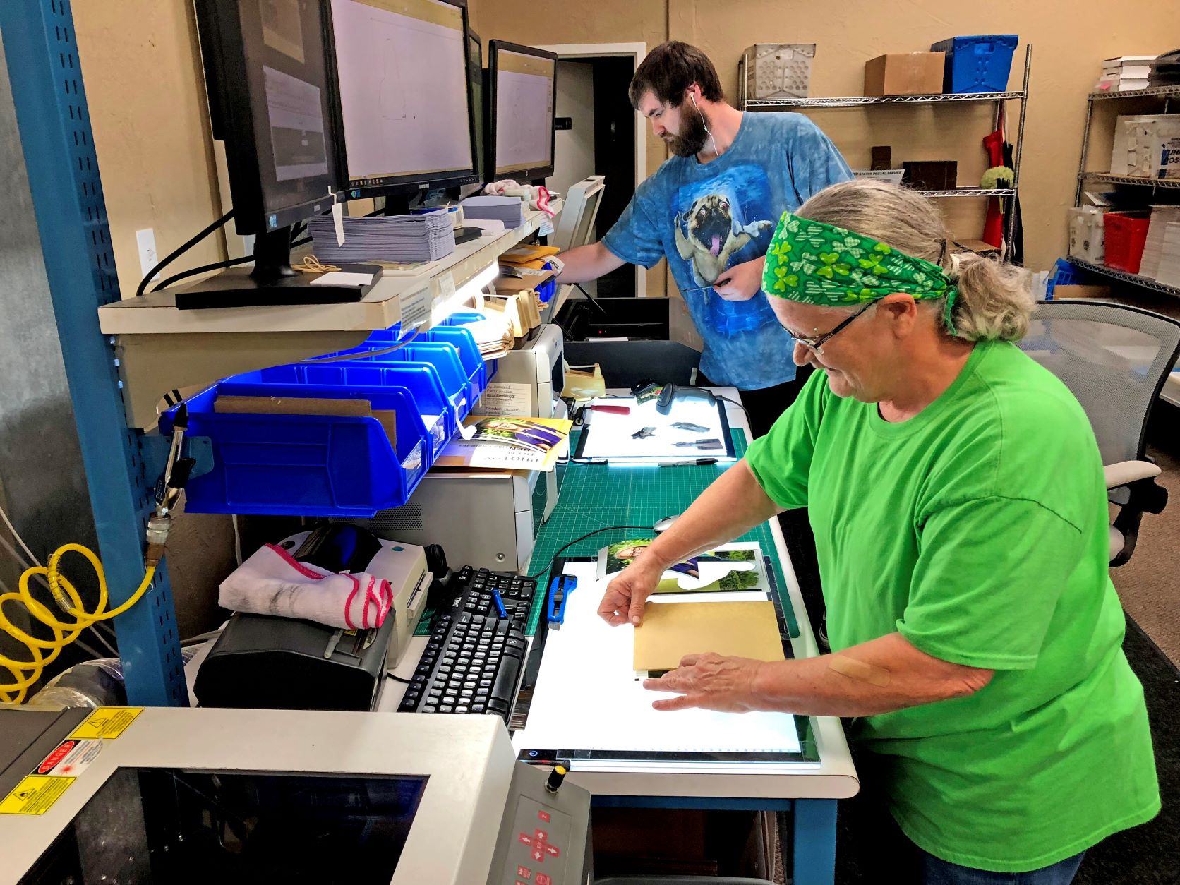 Two employees checking and handling photo products at workstations in Candid’s Royal Lab