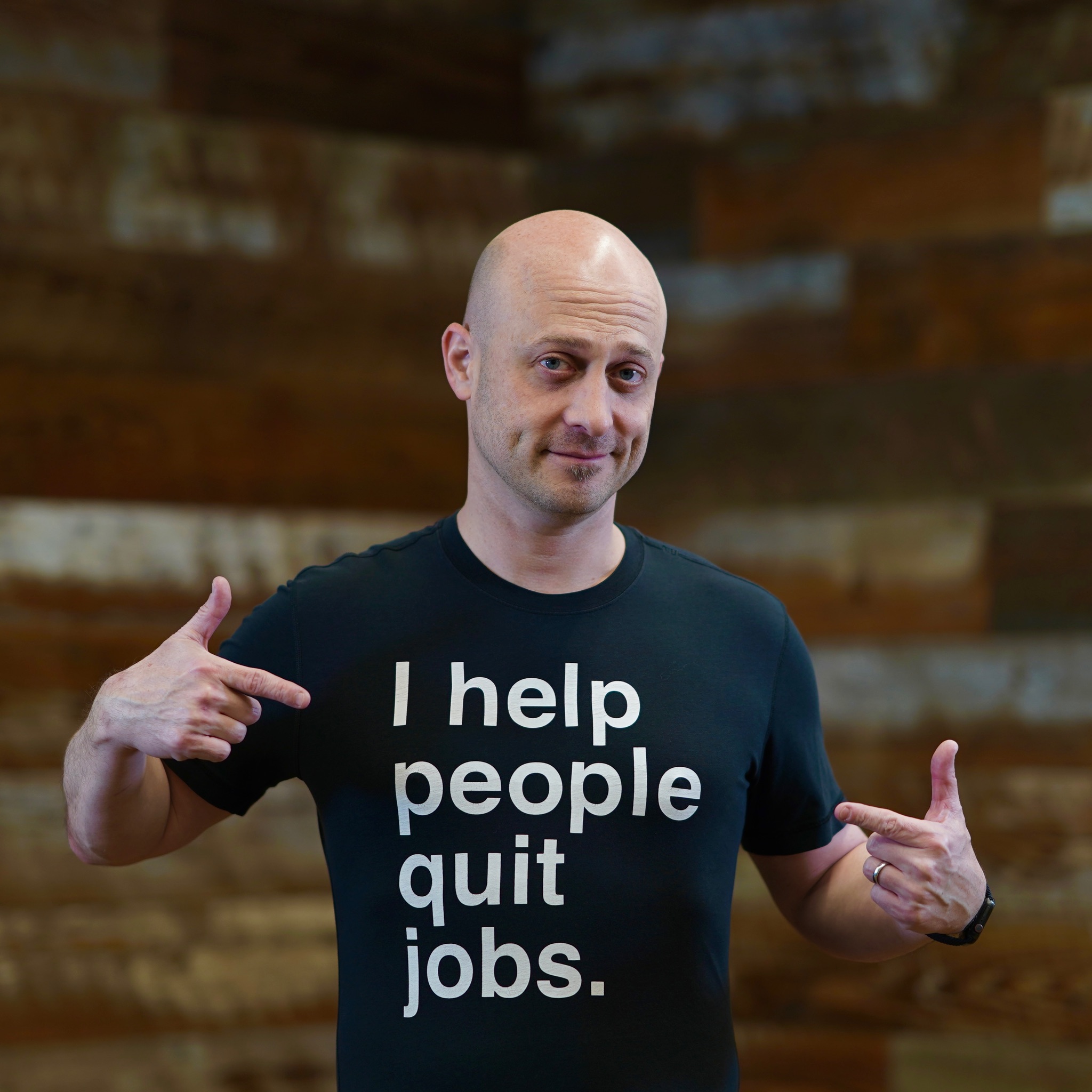 Joshua Baer pointing to his T-shirt, which reads I help people quit jobs