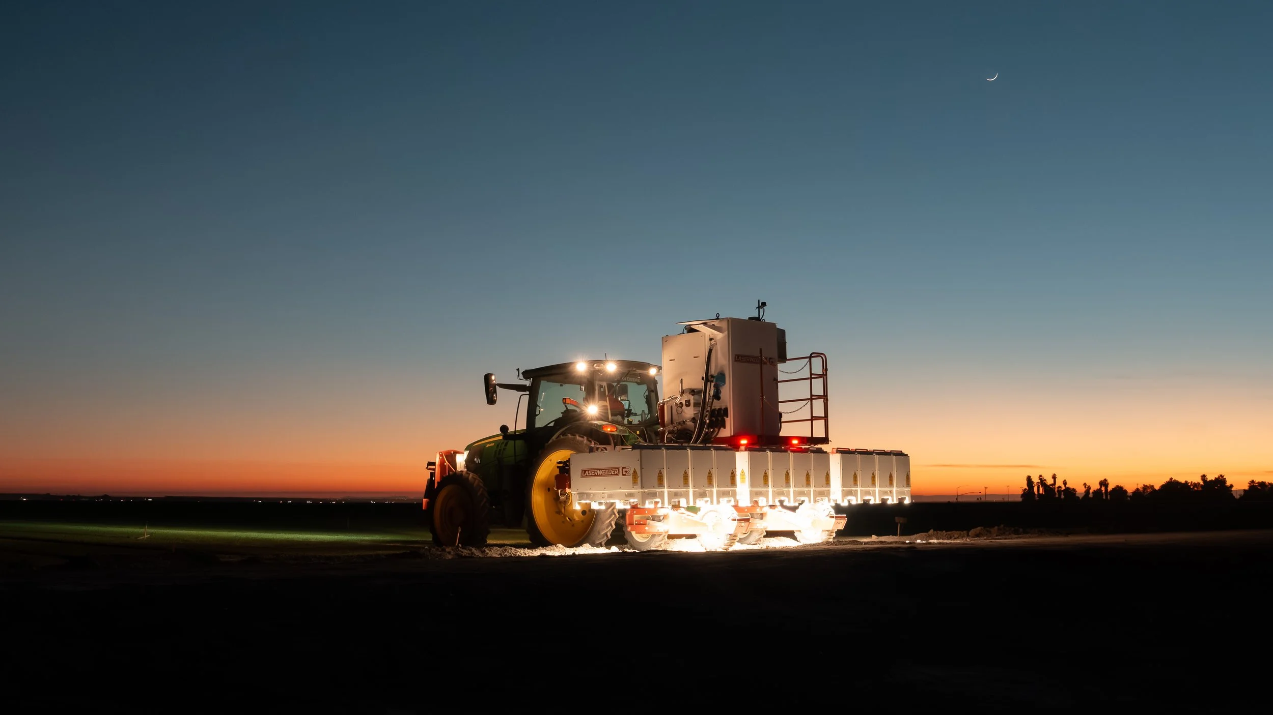 A tractor pulling Carbon Robotics LaserWeeder G2 through a field at sunset