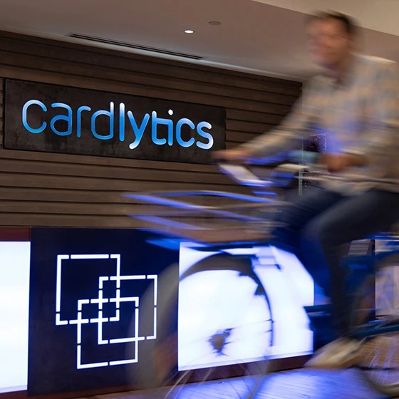 A cyclist passing the illuminated Cardlytics sign in an office photograph from the company’s careers page