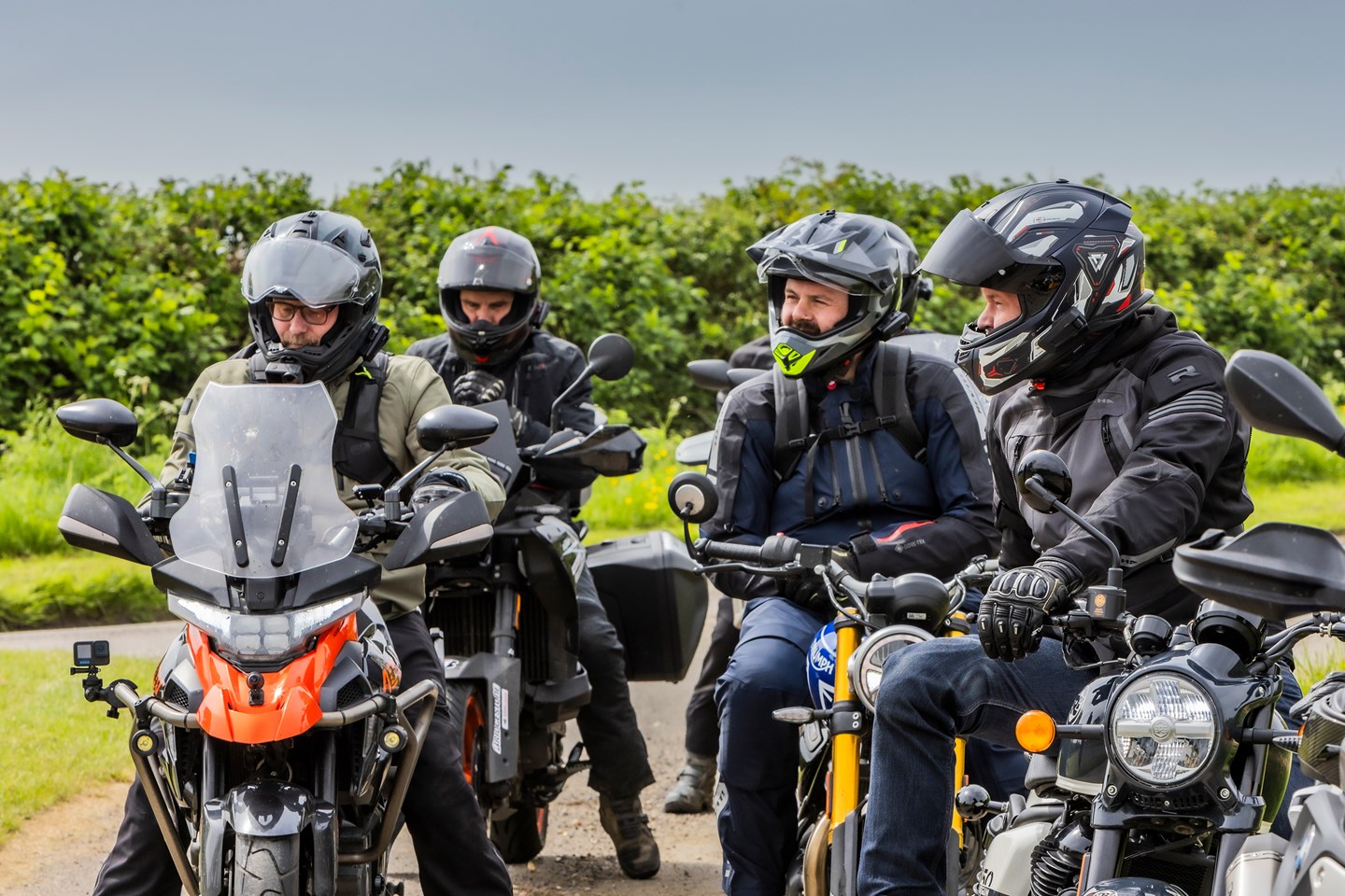 Four motorcyclists wearing helmets fitted with communication units stand beside their bikes