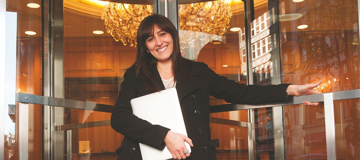 Caren Maio holding a laptop beside glass doors in an archival photograph
