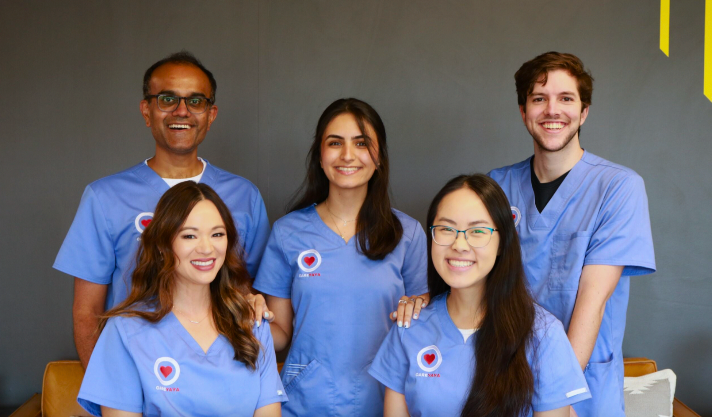 Five CareYaya team members in blue scrubs smile together.