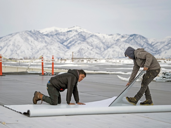 Two workers installing Carlisle roofing membrane with snow-covered mountains behind them