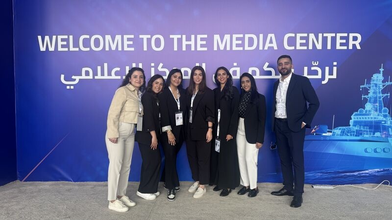 Seven CARMA team members standing in front of an English and Arabic media-centre sign