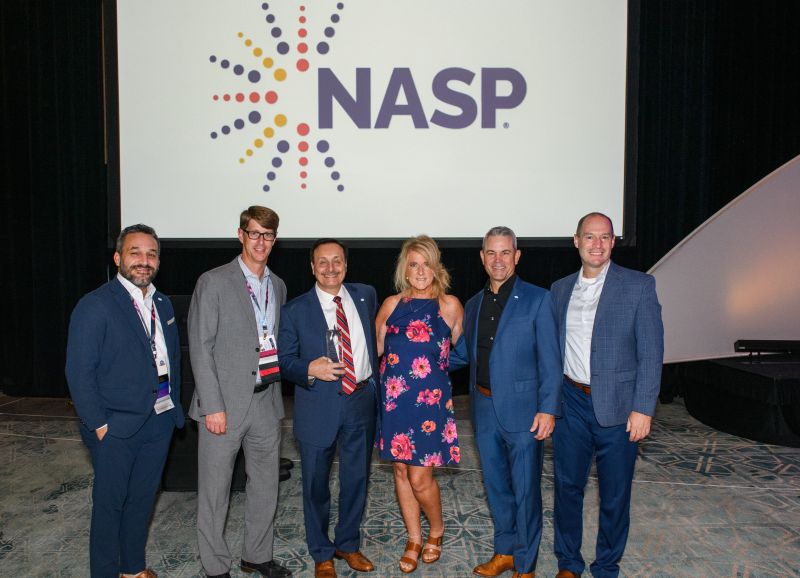 Carmine DeNardo holding a glass award with fellow National Association of Specialty Pharmacy honorees onstage