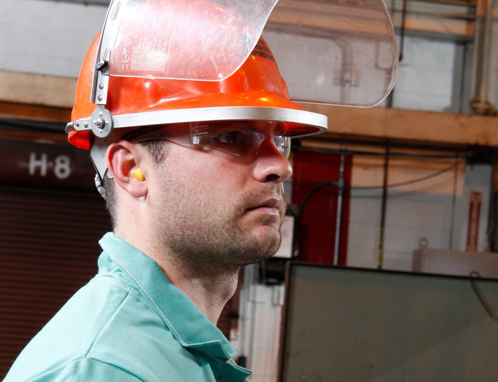 A worker wearing a hard hat, safety glasses, hearing protection and a raised face shield