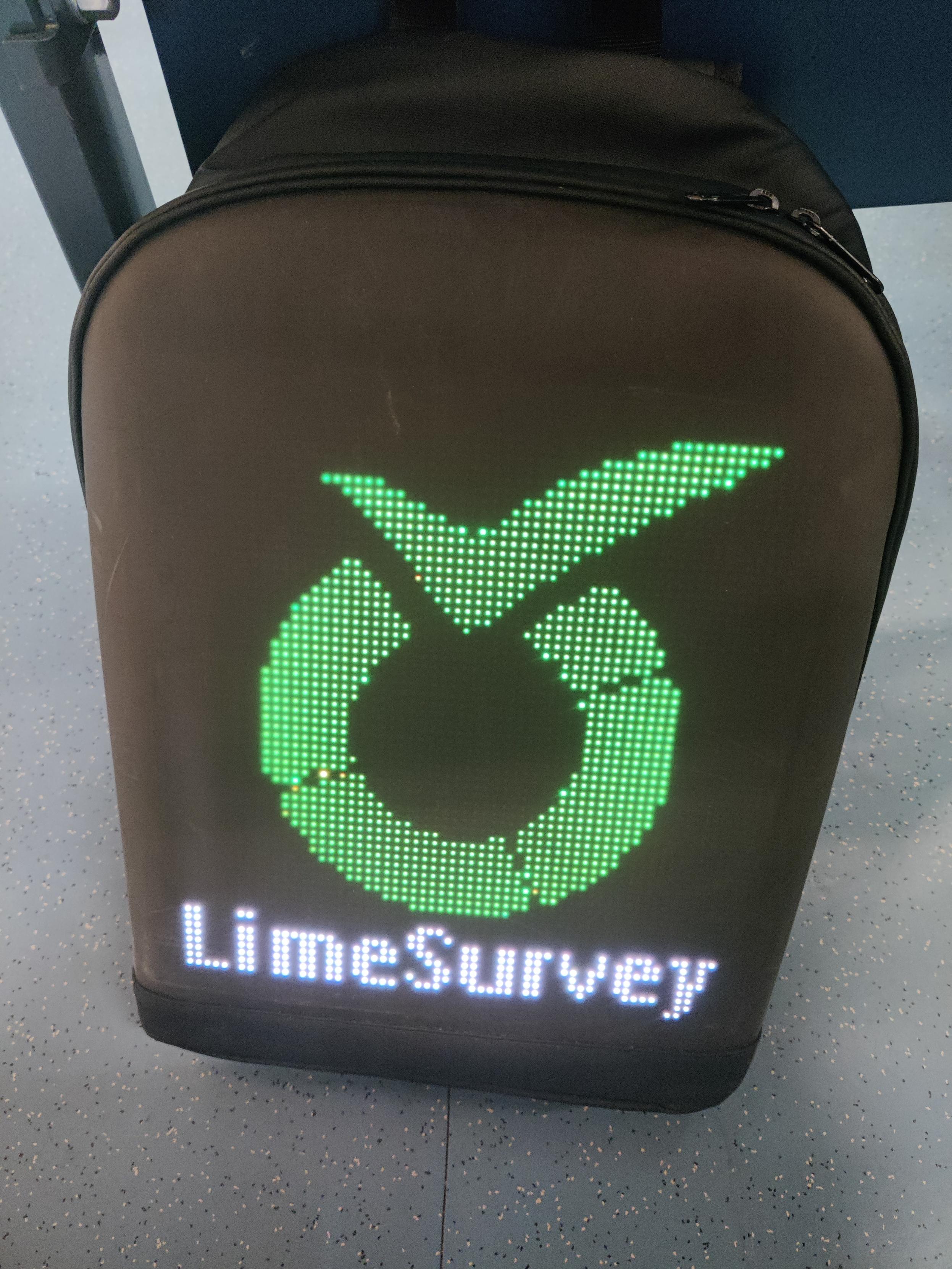 A black backpack displaying a green LimeSurvey logo and white lettering on an LED panel