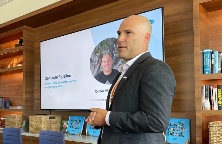 Carter Wigell speaking beside a presentation screen in a room with bookshelves