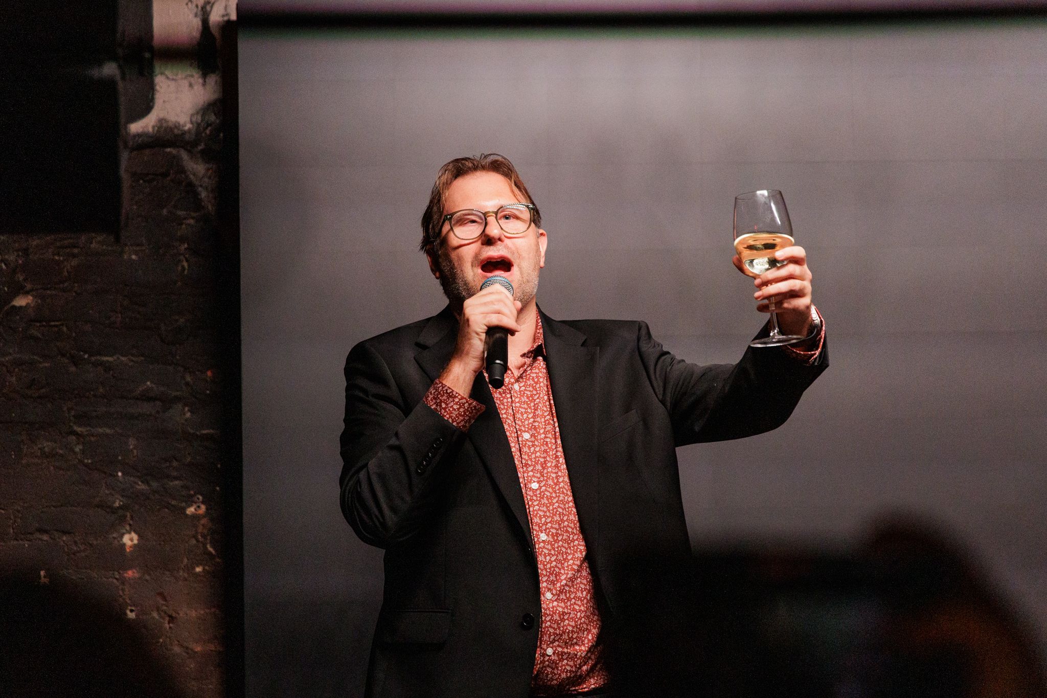 Casey Given holding a microphone and raising a glass at Data After Dark in Washington