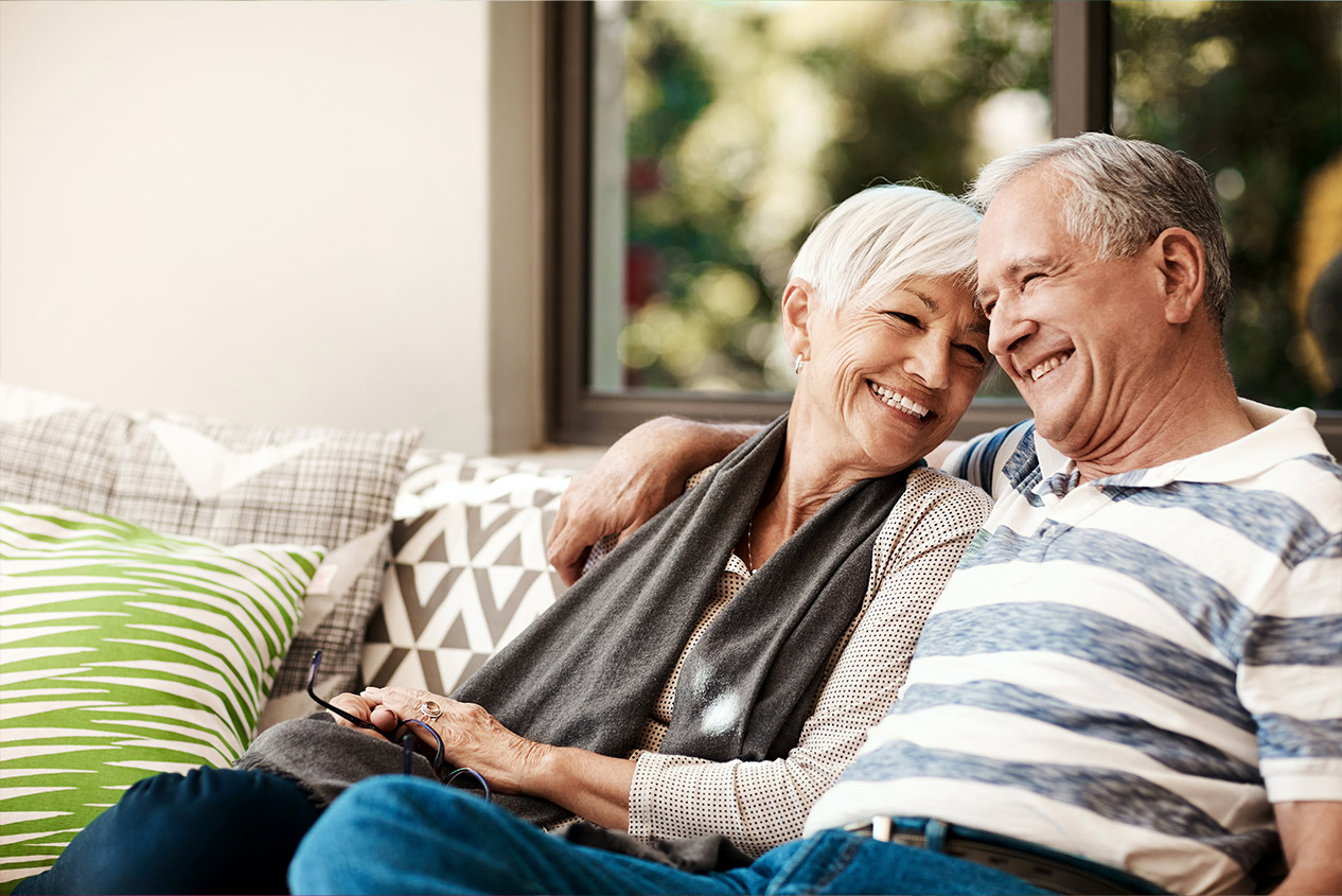 An older couple smiling together on a couch in Cash Store’s installment-loan marketing photograph