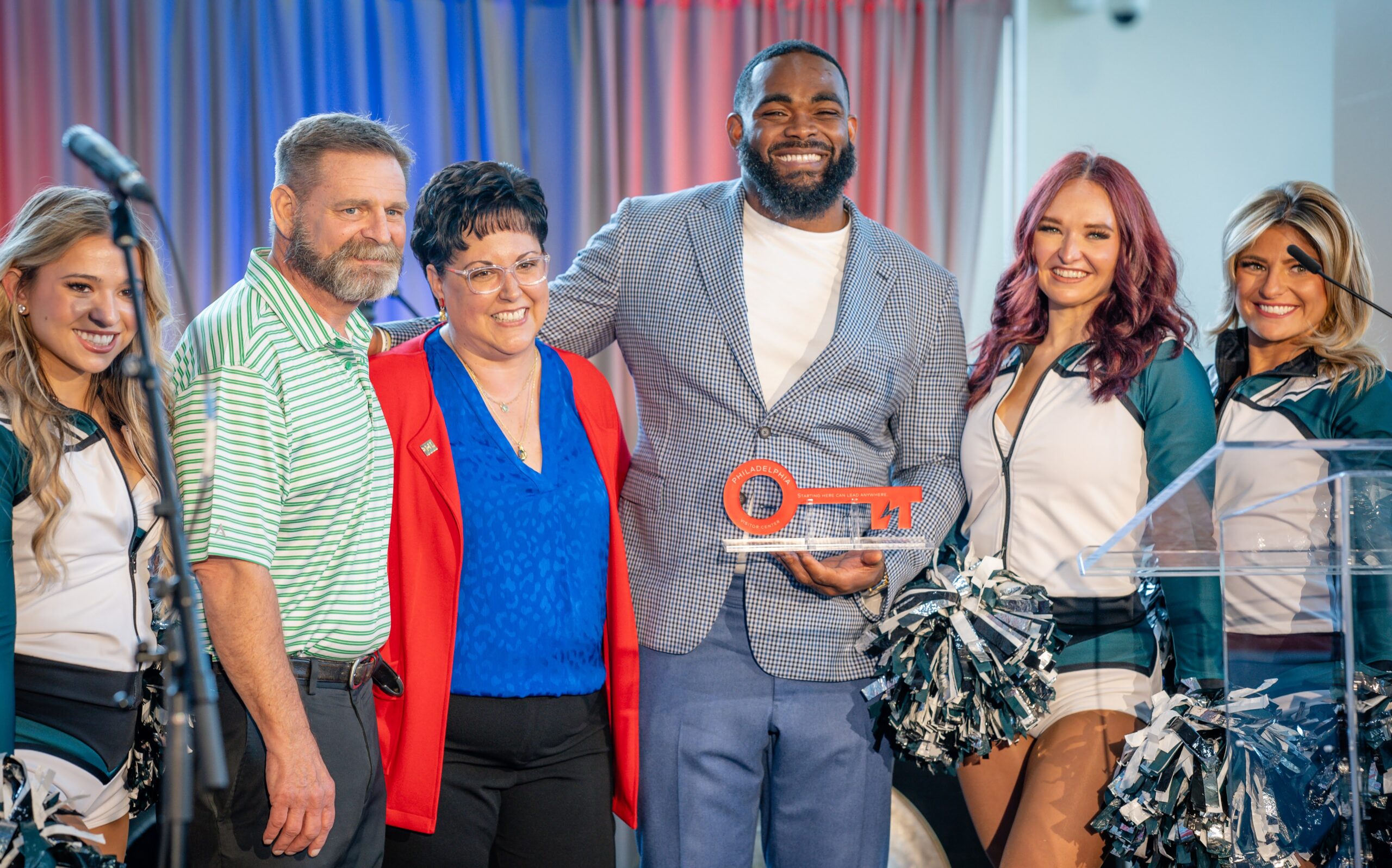 Guests and Philadelphia Eagles cheerleaders gather around an award at a Cashman and Associates event