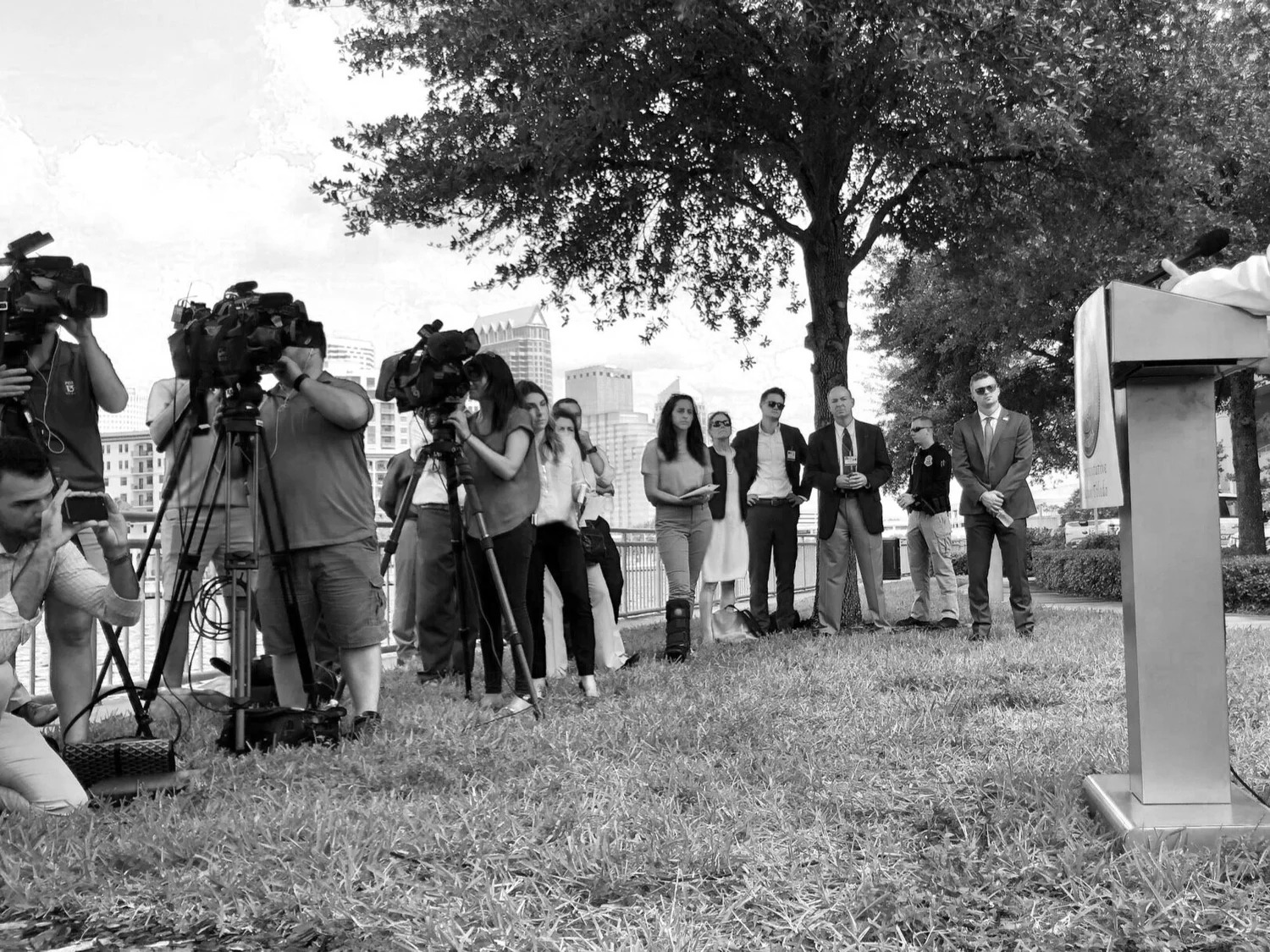 News cameras and a crowd gathered around speakers at an outdoor media event