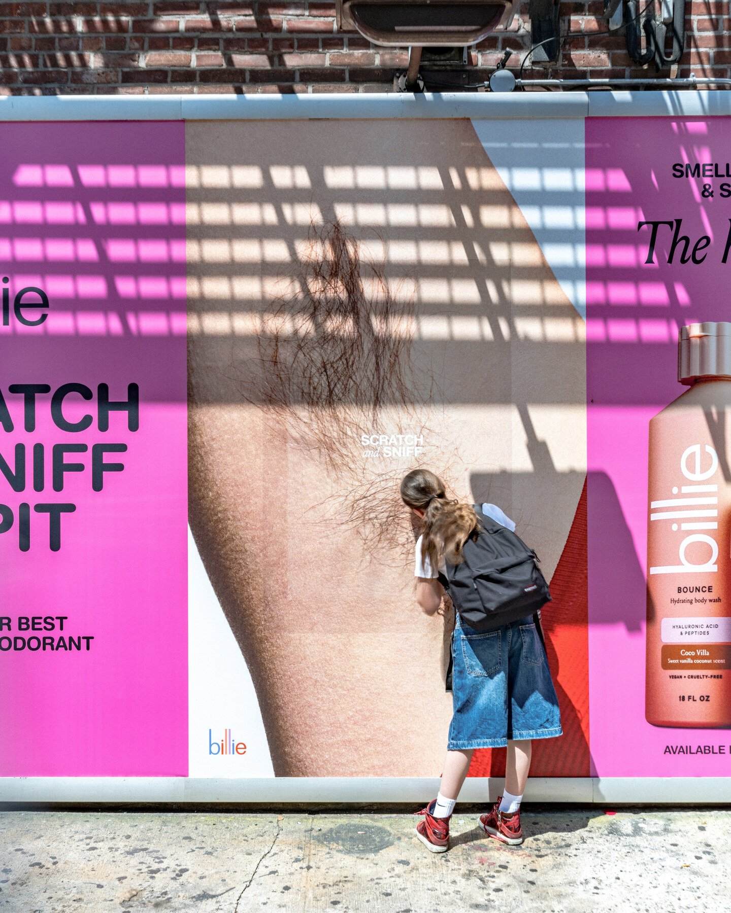 A passerby leans toward a large pink Billie scratch-and-sniff billboard in New York City