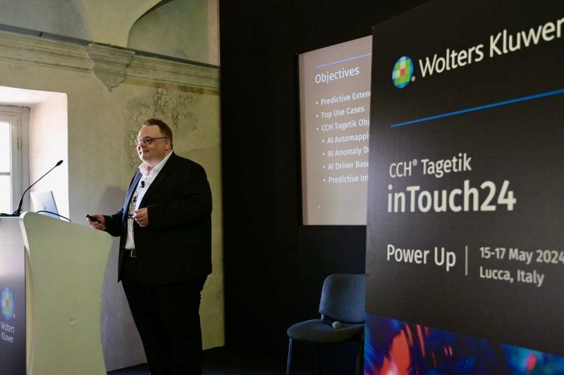 A presenter speaks beside a CCH Tagetik inTouch24 sign at the Lucca conference
