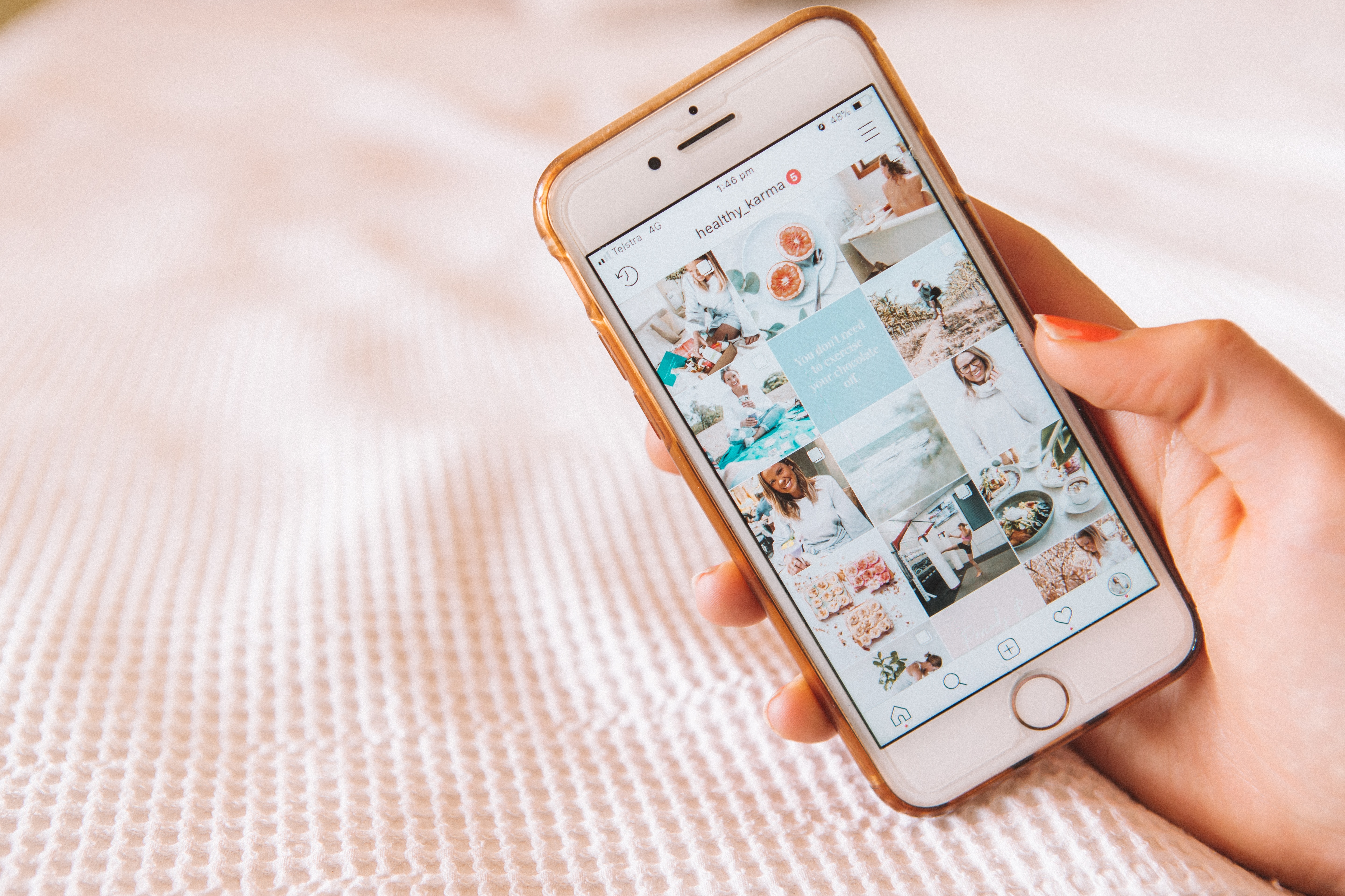 A hand holding a phone displaying a social media image grid