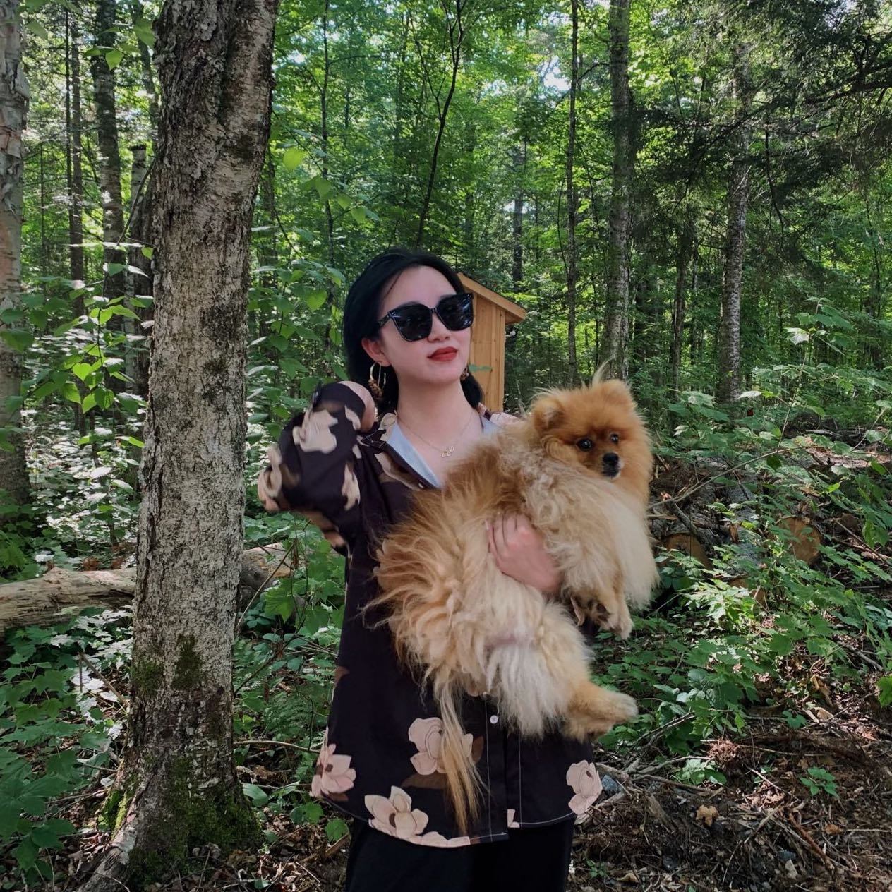 Cecilia Cai outdoors among trees, holding a small fluffy dog