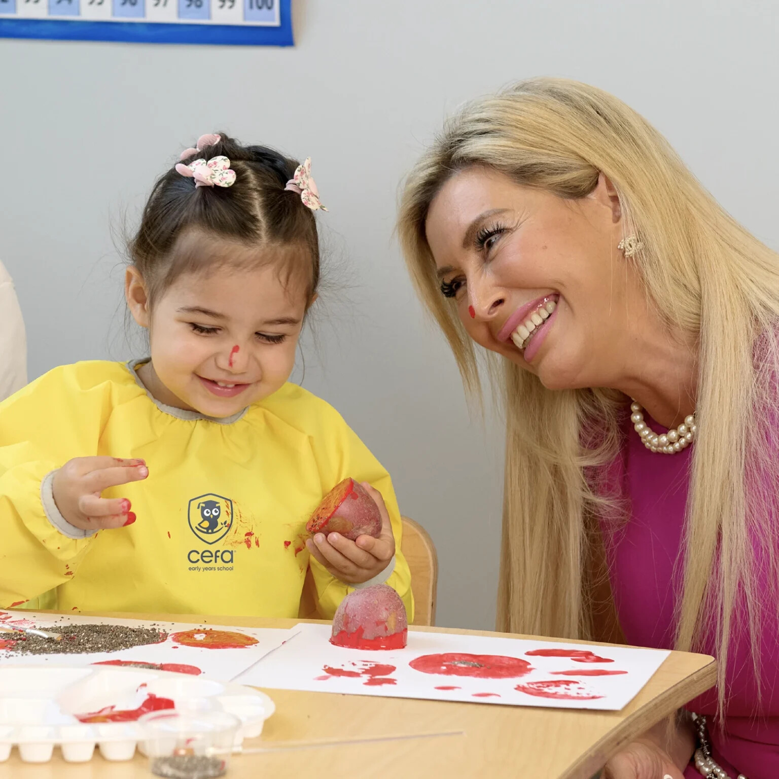 Natacha Beim Boserup smiling beside a young CEFA student making a red paint print