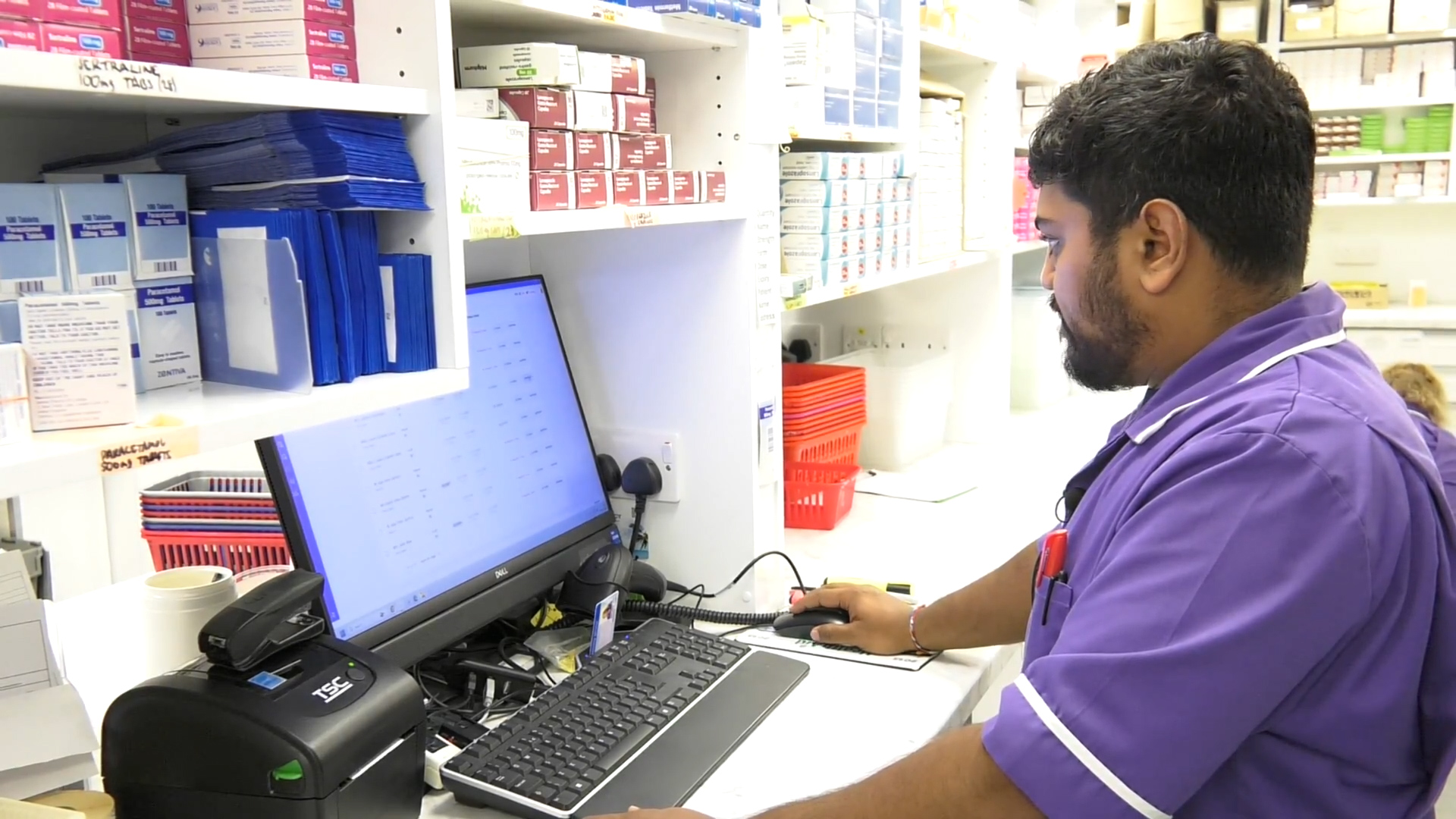 A Nimo Pharmacy team member working at a dispensary computer surrounded by medicine shelves