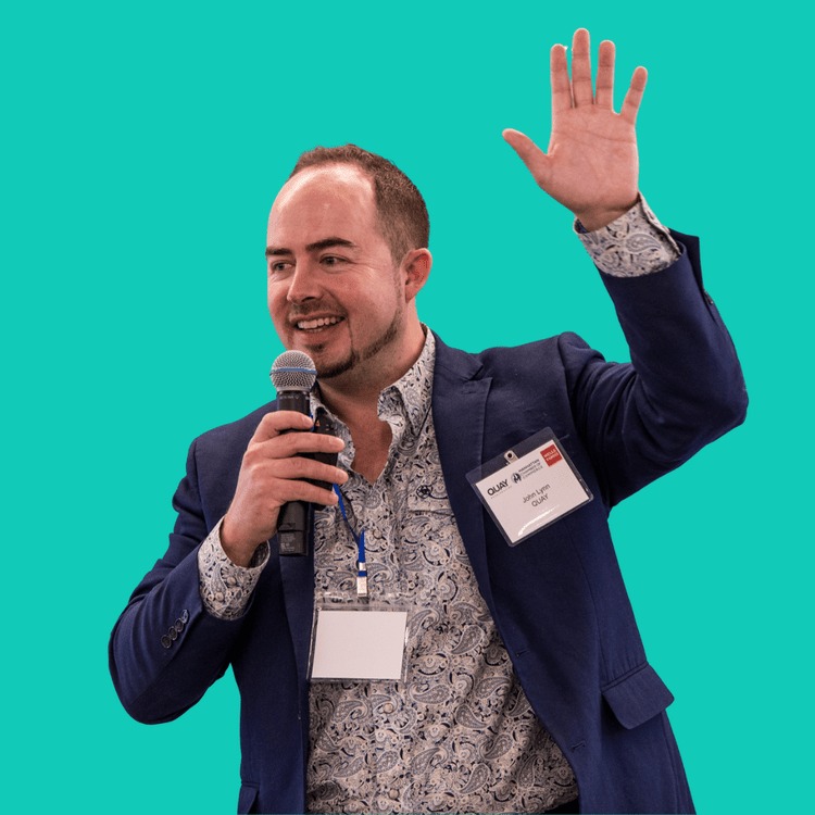 John Lynn holding a microphone with one hand raised