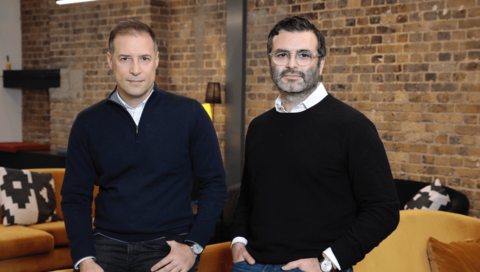 Plentific co-founders Emre Kazan on the left and Cem Savas on the right, standing in a brick-walled office