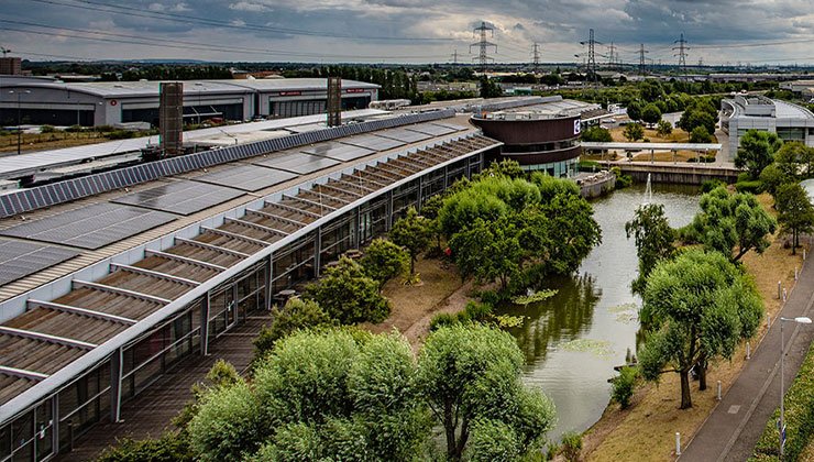 Aerial view of CEME's long campus building, lake, trees and surrounding industrial landscape