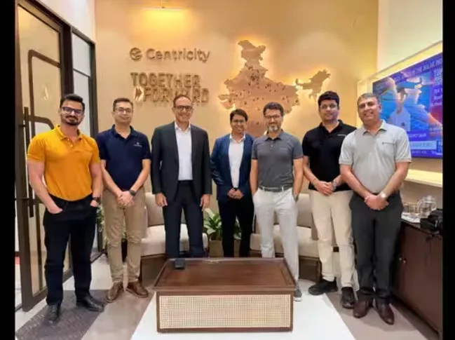 A group poses in Centricity’s office beneath a map of India