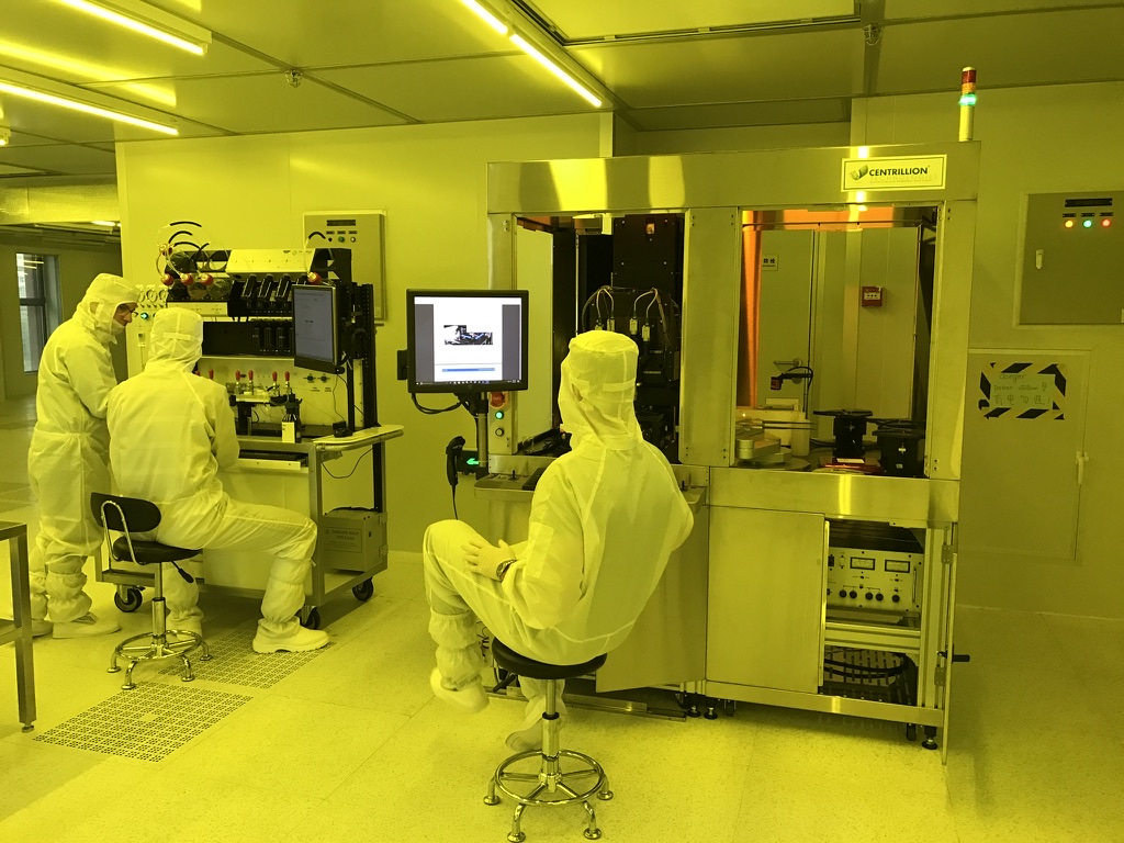 Three Centrillion team members operating equipment inside a yellow-lit cleanroom