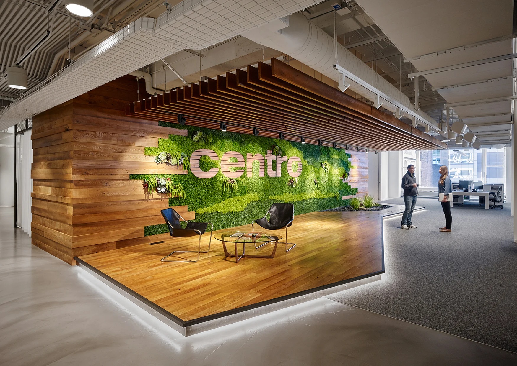 Historical Centro office with a green planted wall, wooden seating platform, and two people talking