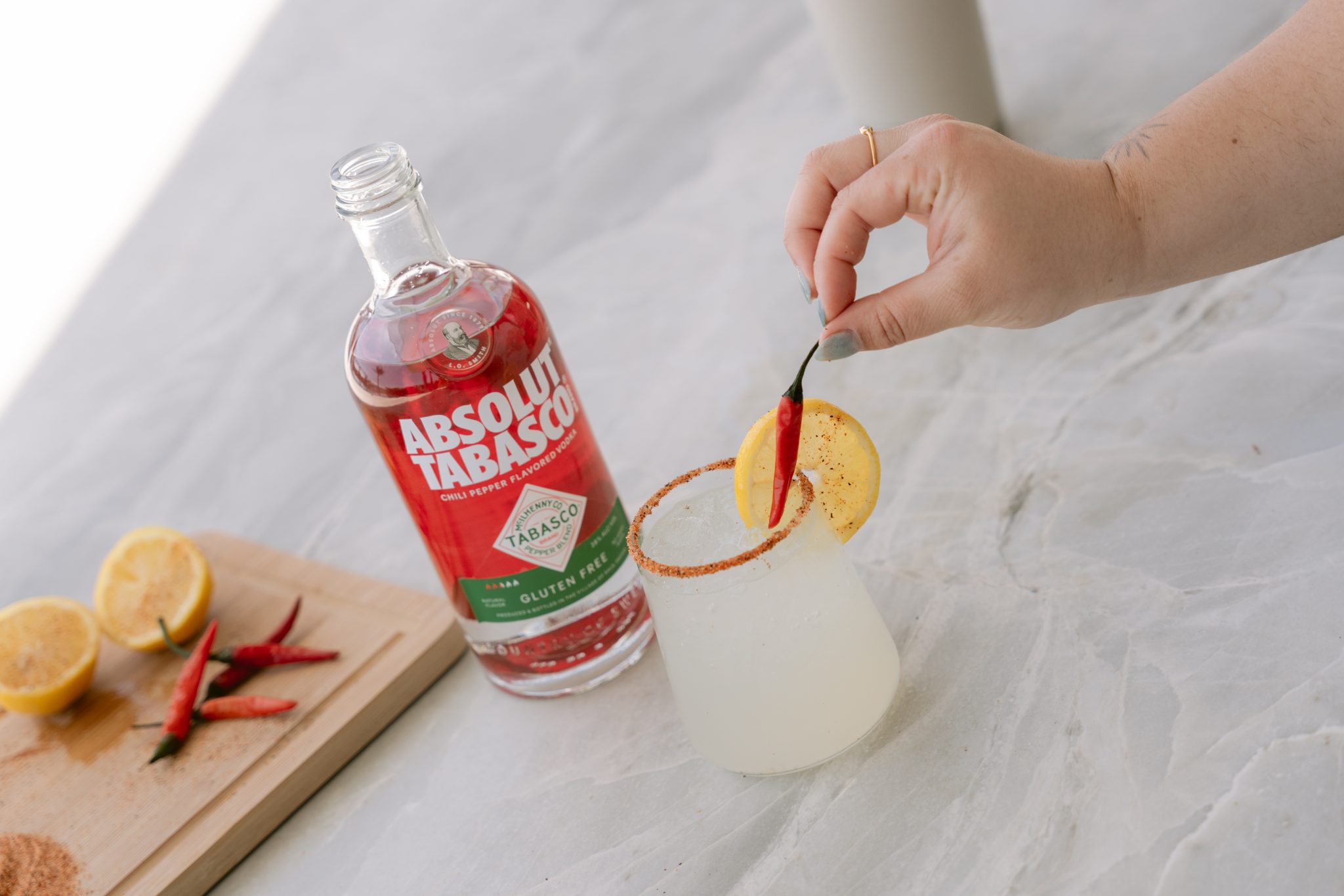 A hand garnishes a spicy cocktail beside a bottle of Absolut Tabasco at CBC's Culinary House West