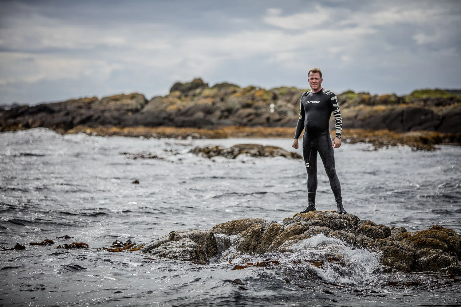 Chad Anderson in a wetsuit standing on rocks at the Islay shoreline