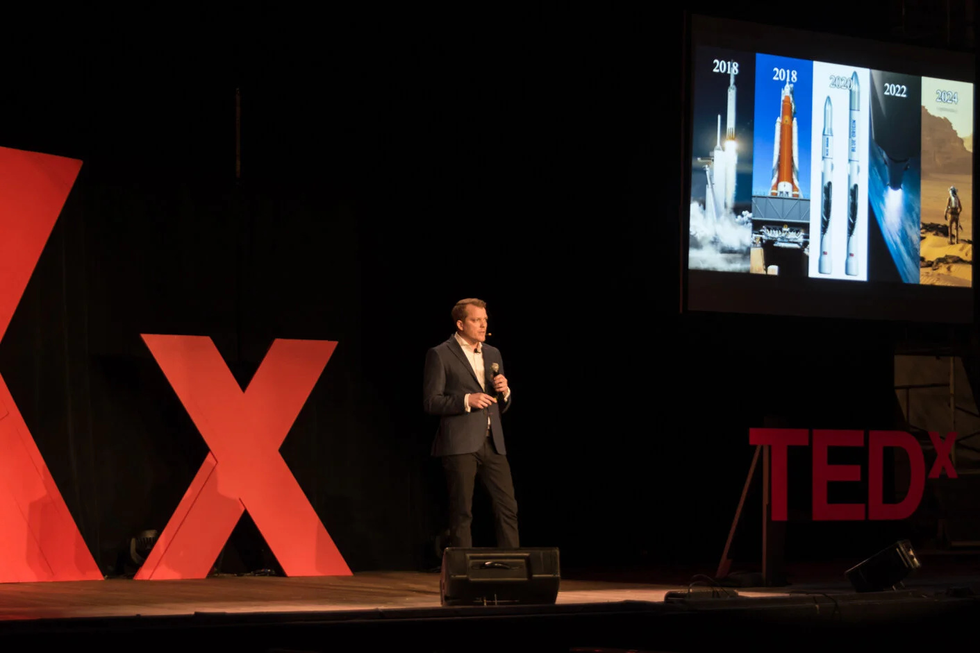 Chad Anderson speaking on a TEDx stage beside a presentation about space