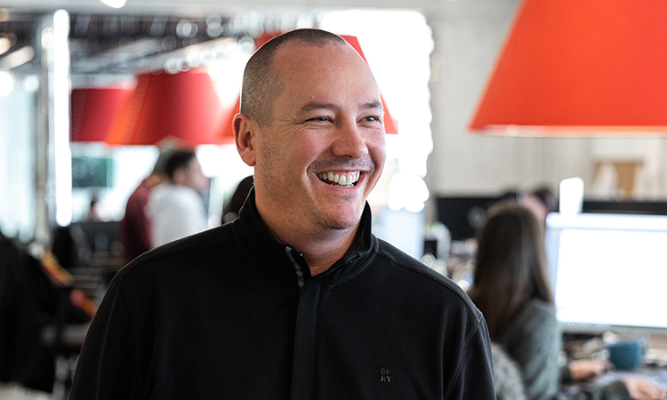 Chad Hetherington smiling in an office with desks and orange lamps