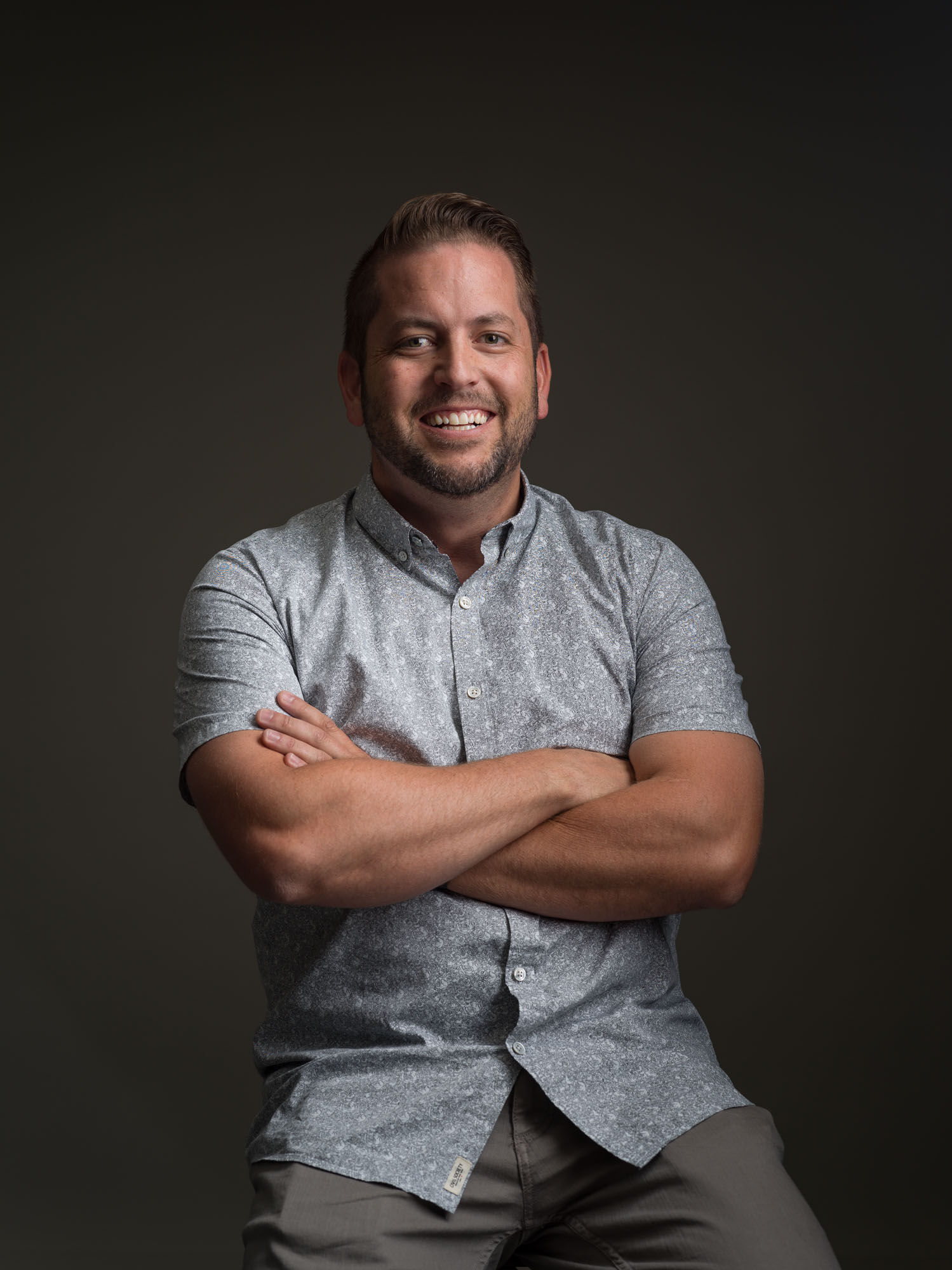 Chad Sollis seated against a dark studio background, smiling with his arms folded