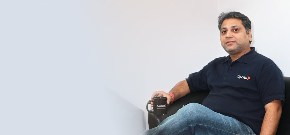 Chaitanya Jawale seated in a chair, wearing an Opcito polo shirt and holding a company mug