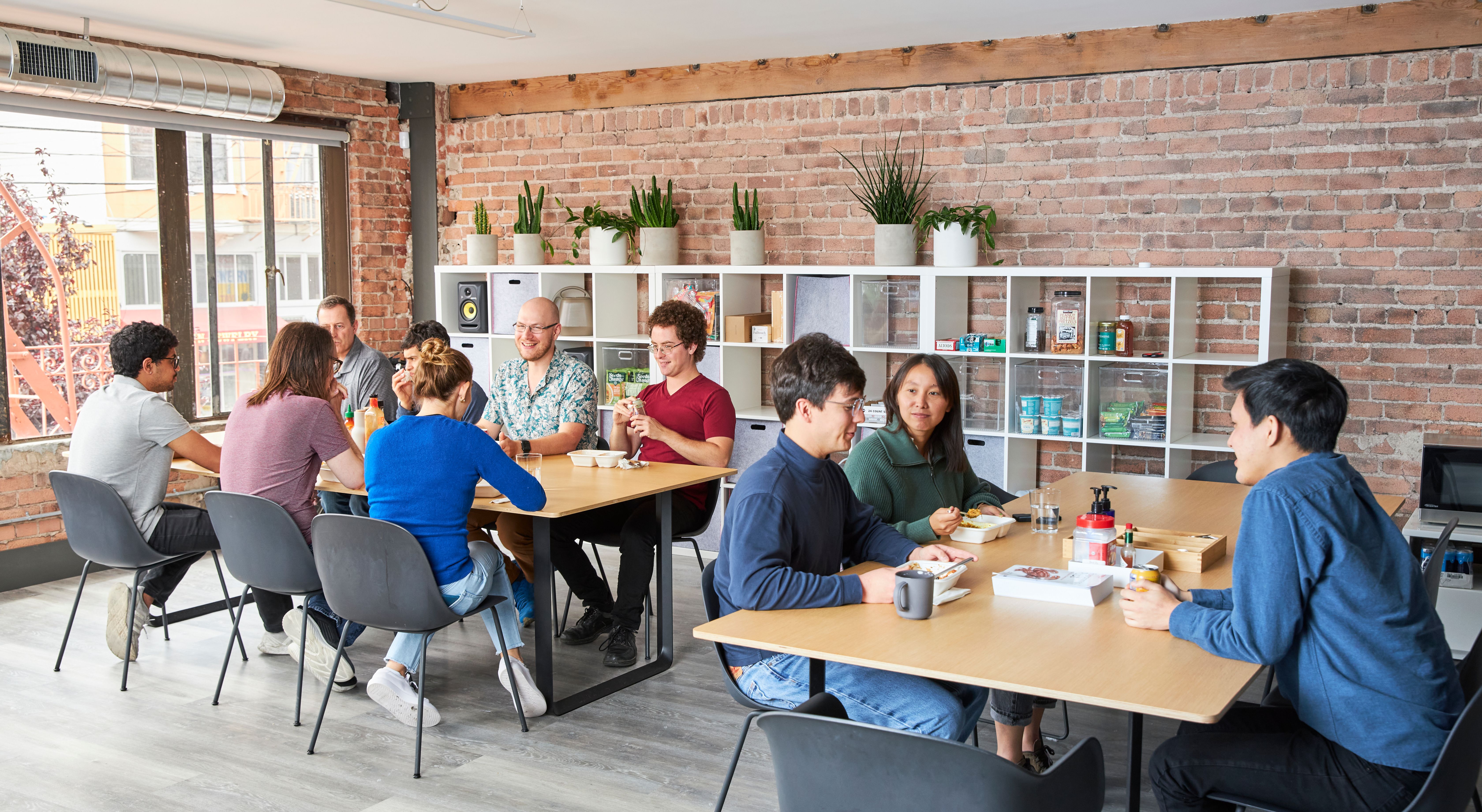 Members of the Chalk team having lunch around two tables in a brick-walled office