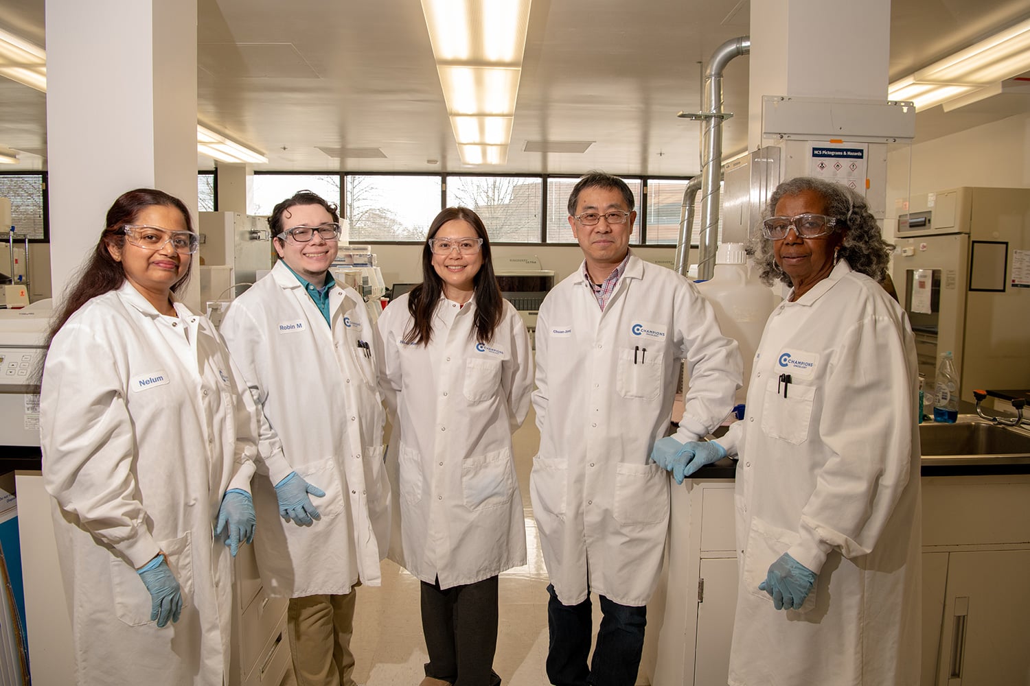 Five Champions Oncology laboratory team members wearing protective glasses and lab coats