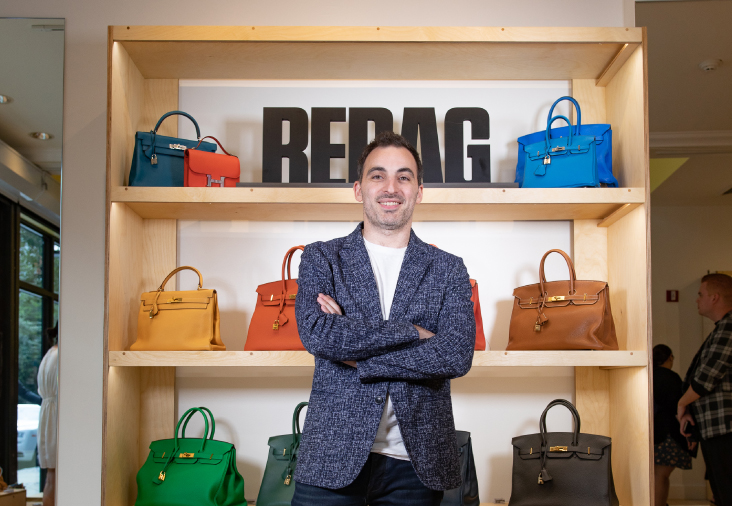 Charles Gorra standing in front of shelves of colorful luxury handbags in a Rebag store