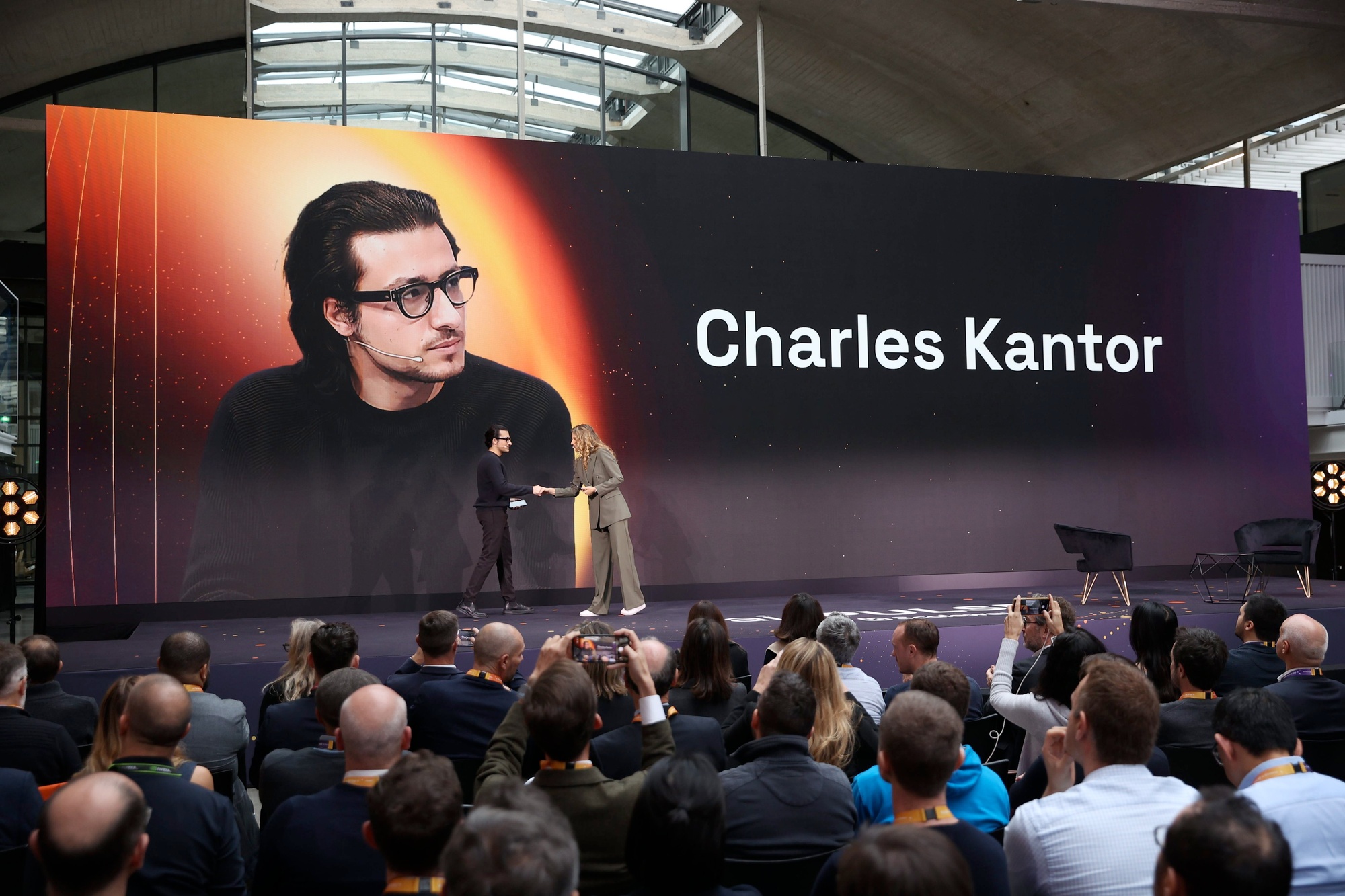 Charles Kantor greeting an interviewer on a conference stage in front of an audience