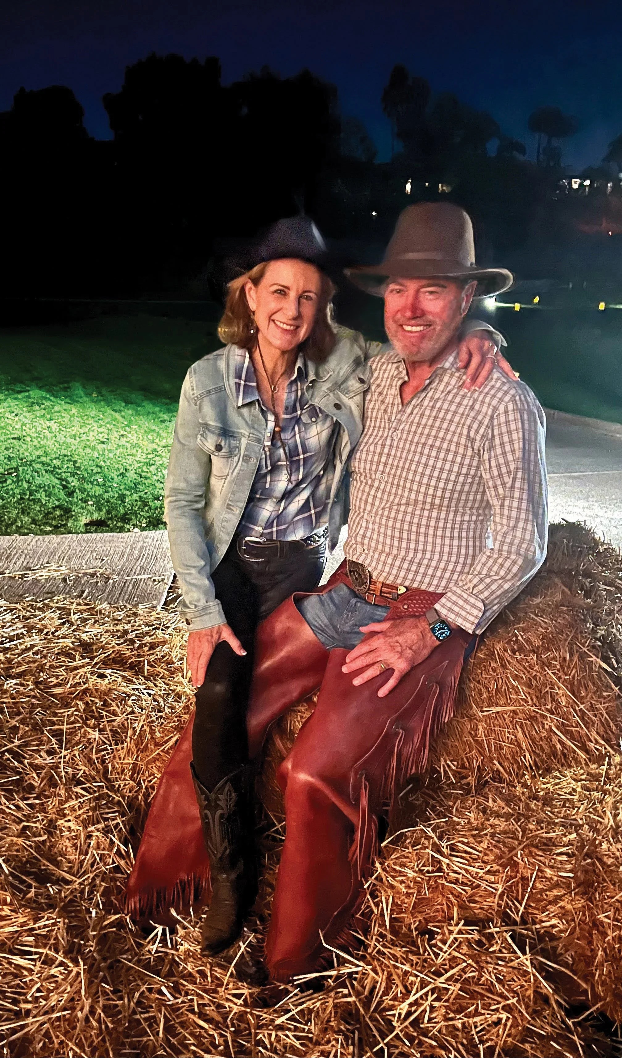 Charles and Cheryl Reynolds dressed in Western clothes, seated together on hay bales at night