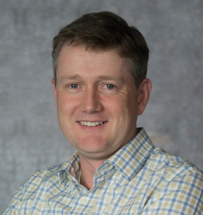 Charles Teague smiling in a checked shirt in a press portrait